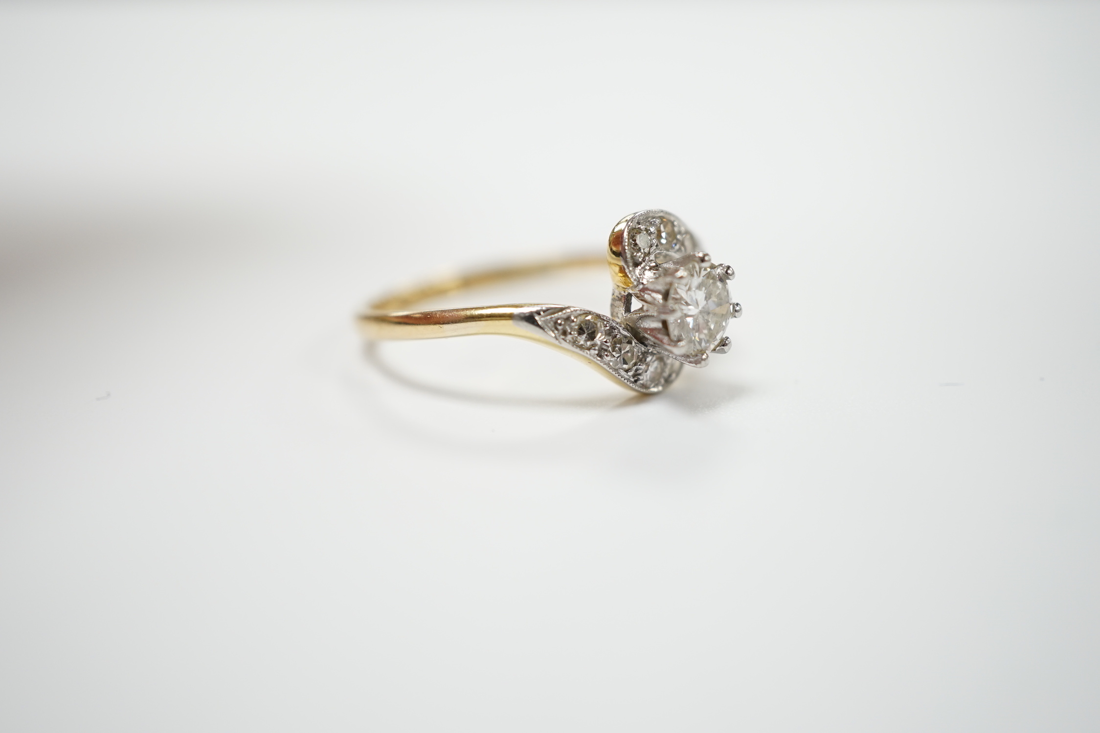 An 18ct, plat and single stone diamond set ring, with diamond chip set crossover shoulders, size P/Q, gross weight 3.1 grams.